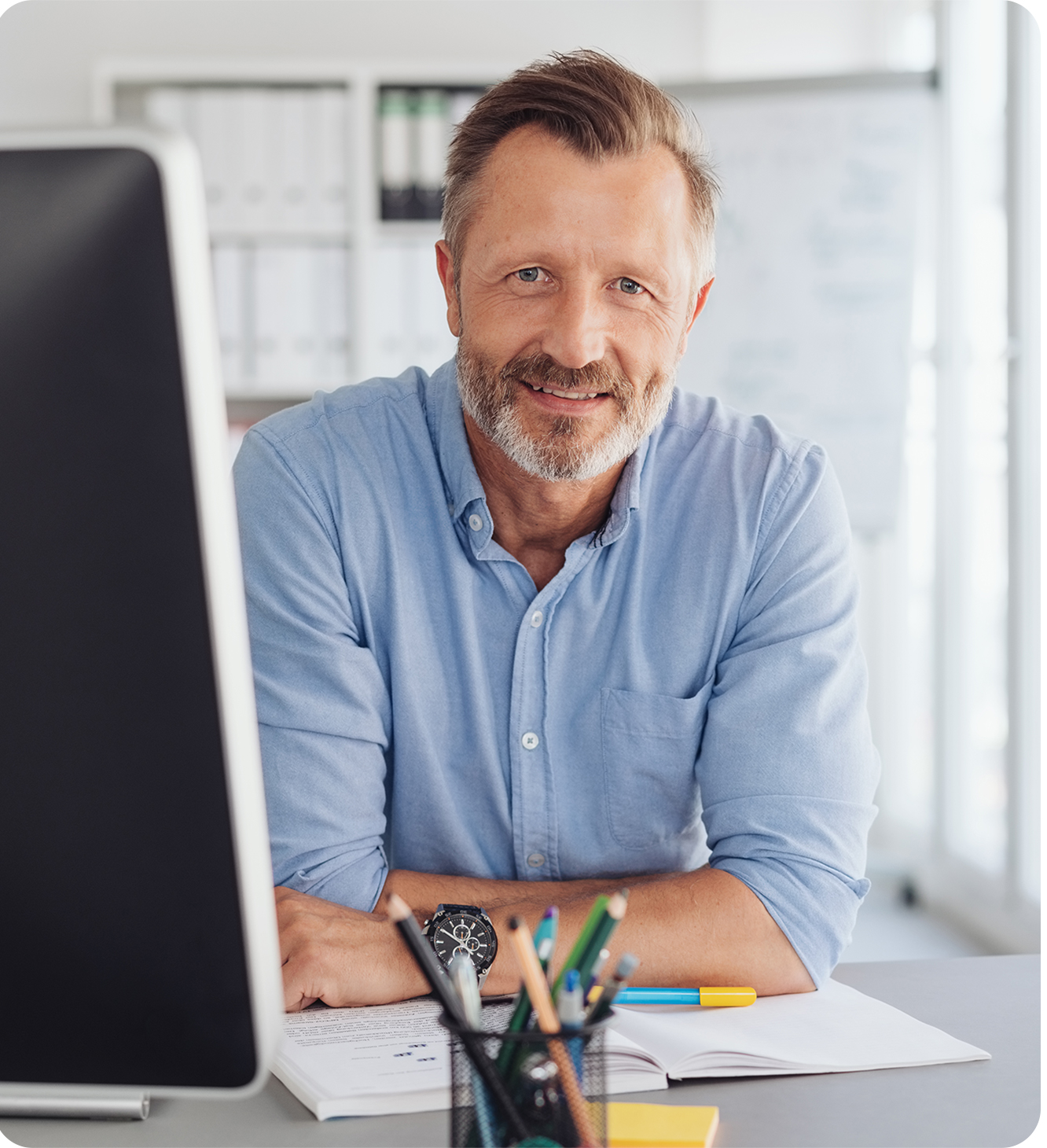 older online male teacher smiling in front of a desktop